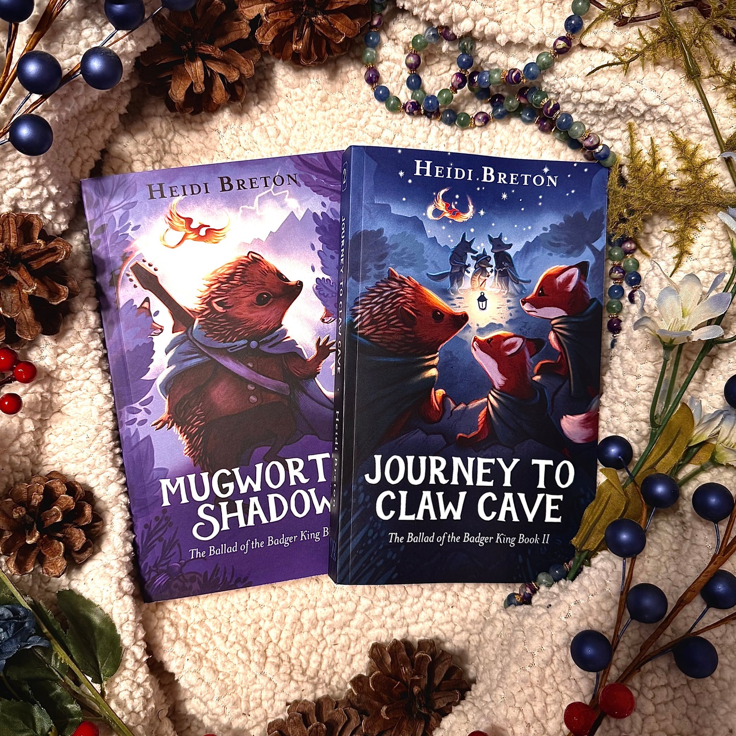 Two books titled 'Mugwort's Shadow' and 'Journey to Claw Cave' by Heidi Breton on a textured surface with decorative elements.