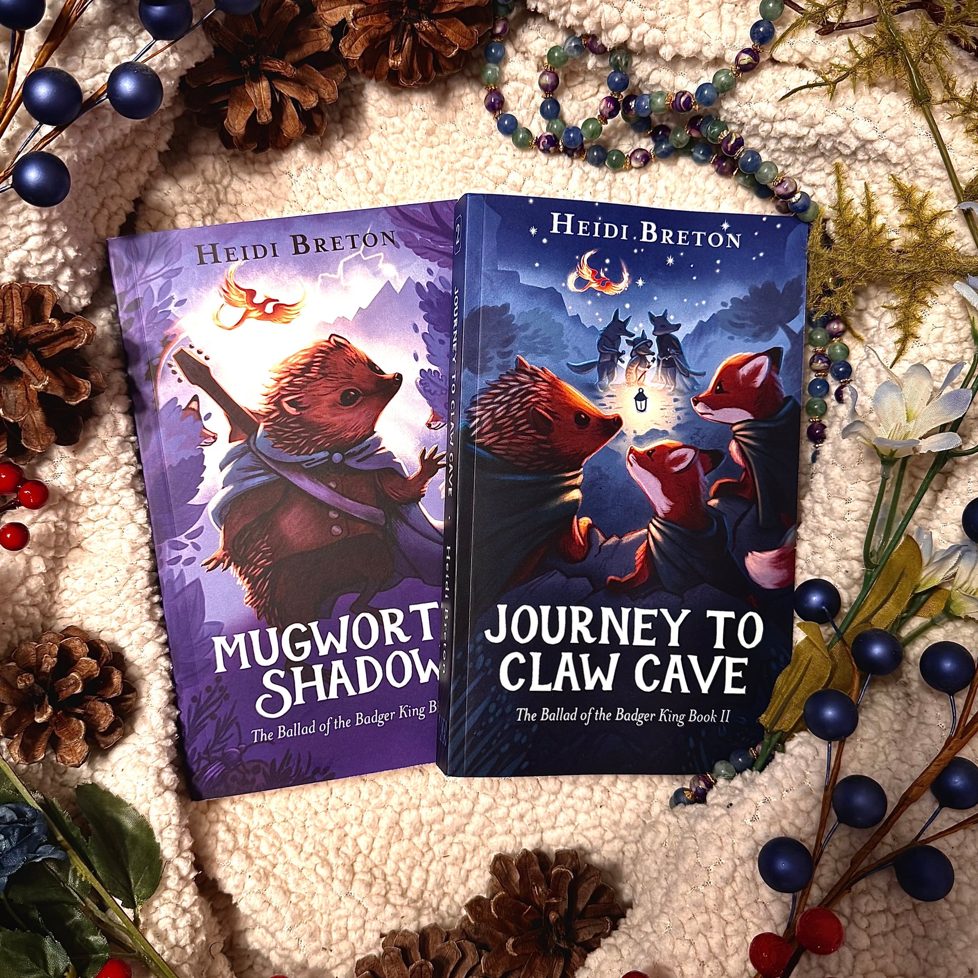 Two books titled 'Mugwort's Shadow' and 'Journey to Claw Cave' by Heidi Breton on a textured surface with decorative elements.